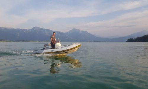 Segellehrer auf dem Elektro-Motorboot vor der wunderschönen Alpenkulisse und Schloss Neuschwanstein