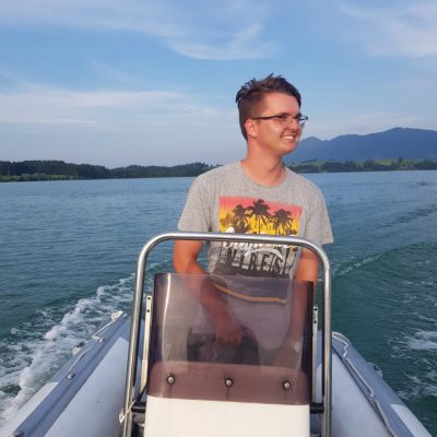 Motorbootlehrer Julian fährt im Elektroboot über den leeren See und strahlt dabei über das ganze sonnengebräunte Gesicht